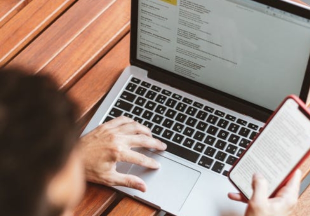 Man scrolling through phone and laptop