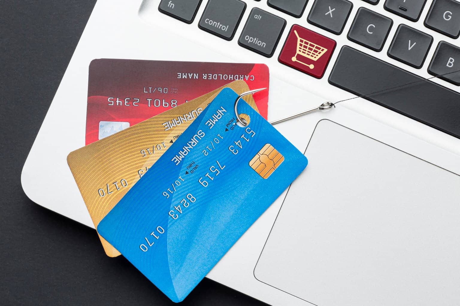 A top view of a laptop with three credit cards on top of it held by a phishing hook